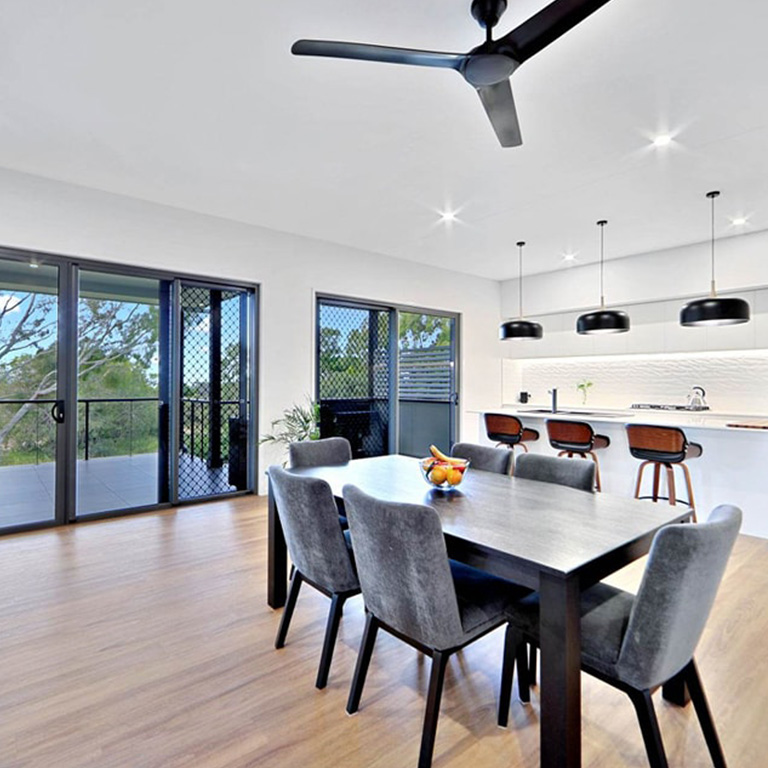 Dining table with grey chairs beside a white kitchen with black pendant lights