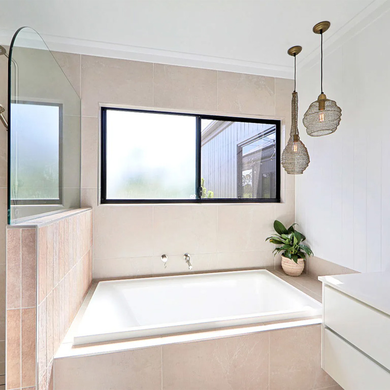 Bathroom with built-in bath under a window, beige tiles and pendant lights